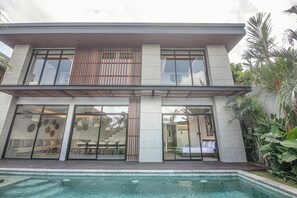 Una casa moderna de dos pisos con amplios ventanales, piscina y un jardín bien cuidado.
