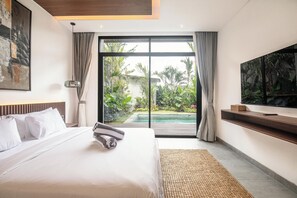 A modern hotel room with a large bed, a flat-screen TV, a view of a swimming pool, and a balcony with plants. - Magnificent 5BR Retreat Near Finns Beach Canggu (Canggu)