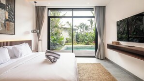 Habitación de hotel moderna con una cama grande, televisión de pantalla plana, vista a una piscina y un balcón con plantas.