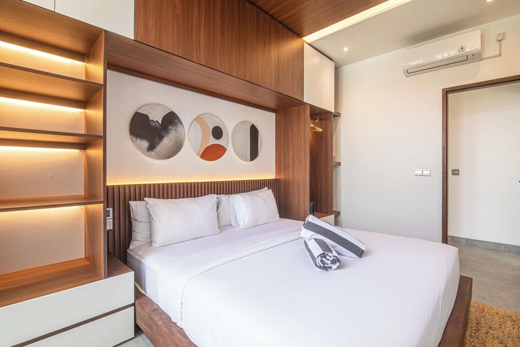 A modern hotel room with a large bed, wooden paneling, and a wall-mounted air conditioner.