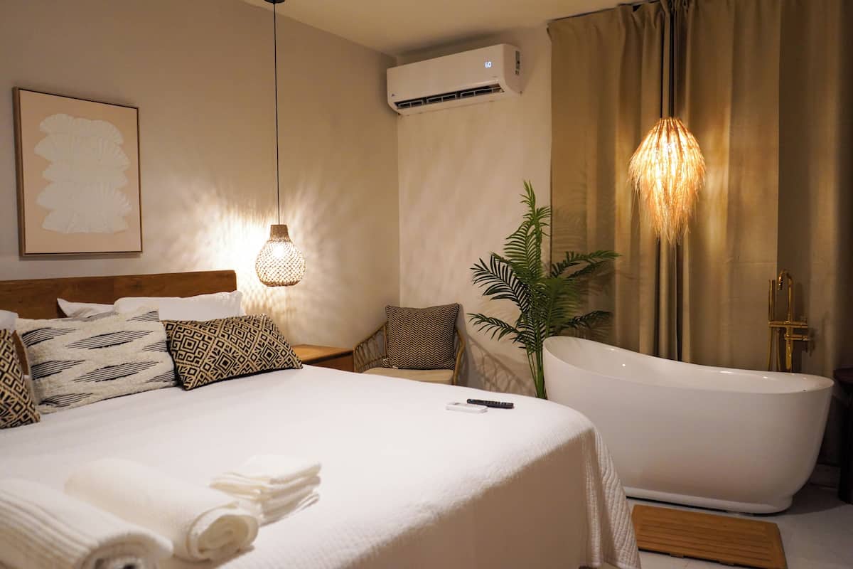 Habitación de hotel con una cama grande, una bañera, una planta en maceta y un aire acondicionado de pared.