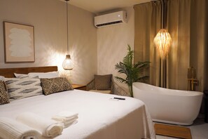 Ein Hotelzimmer mit einem großen Bett, einer Badewanne, einer Topfpflanze und einer Wand-Klimaanlage.