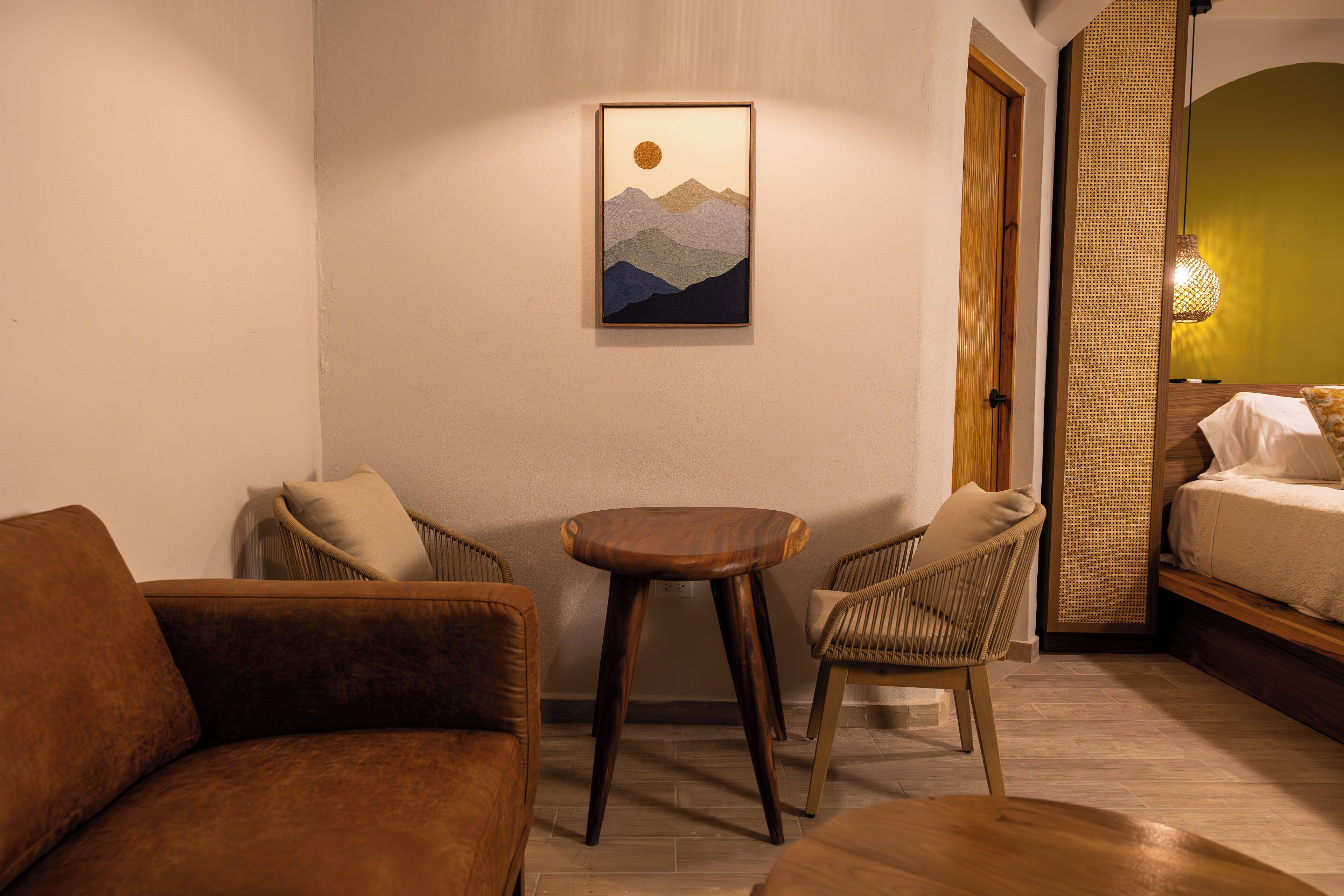 A room with a bed, a sofa, a chair, a small table, and a wall-mounted painting of mountains.