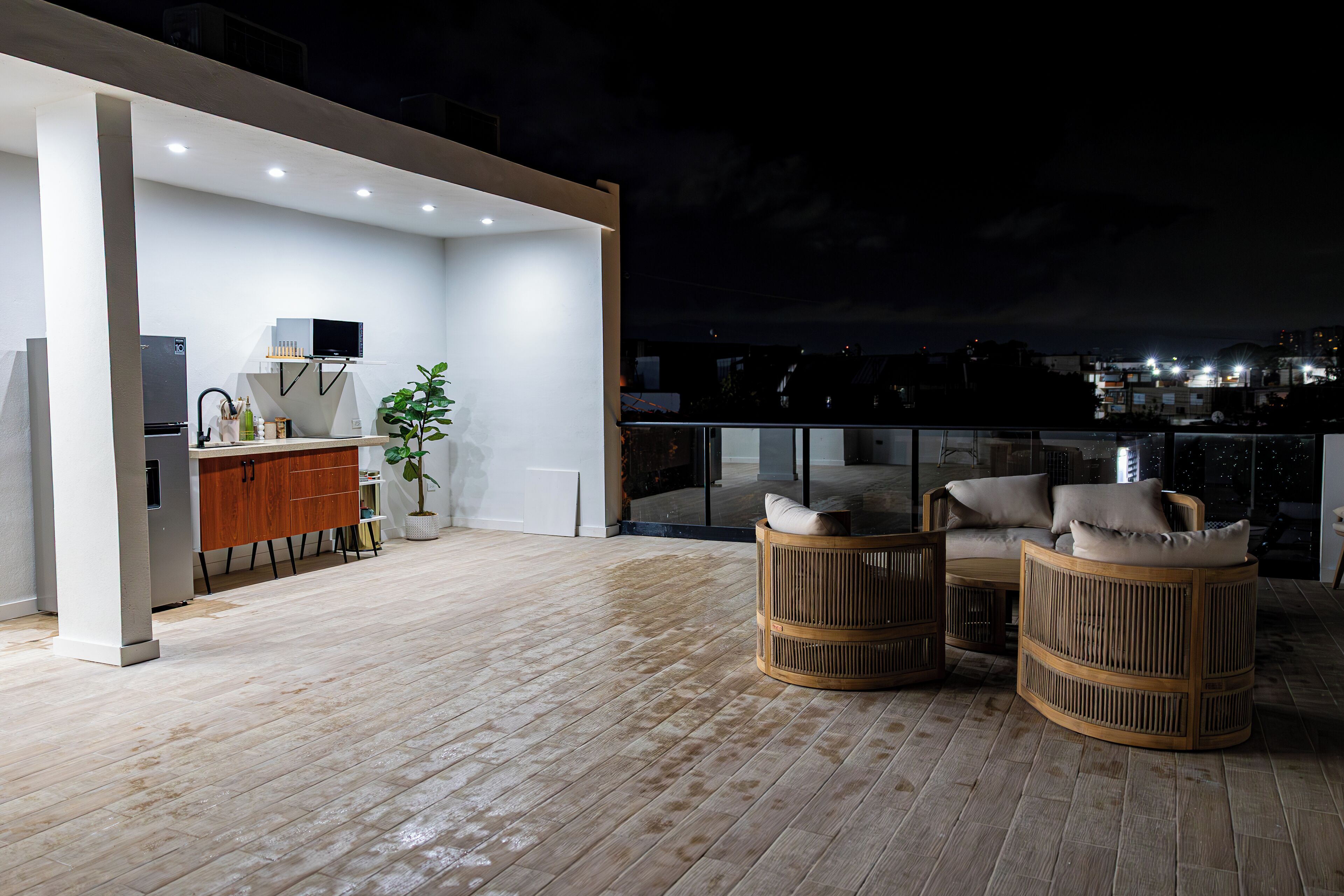 A rooftop terrace with a kitchen area, seating, and a view of the city at night.