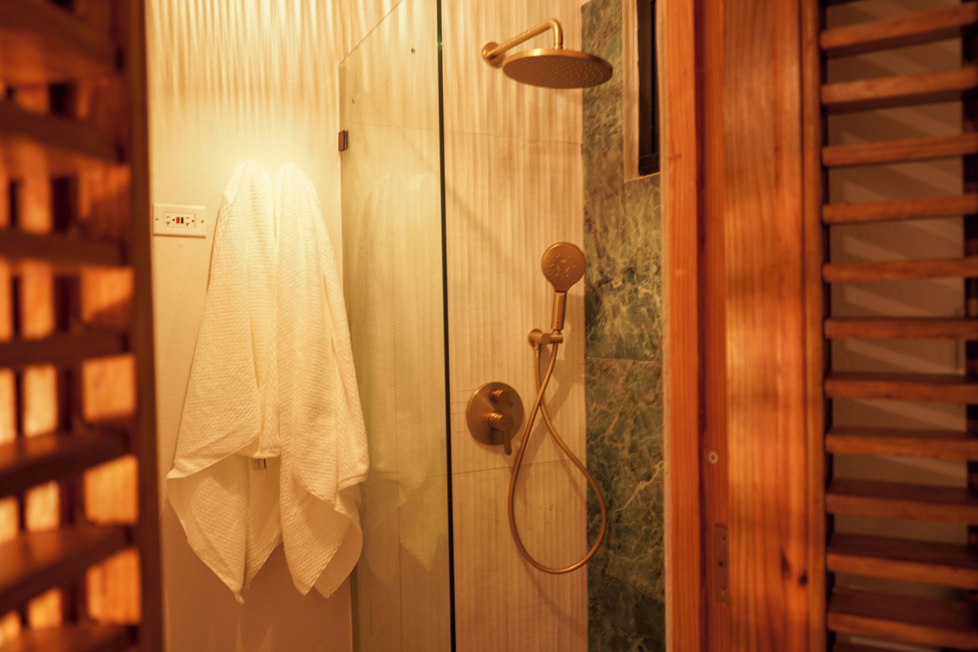 A wooden shower enclosure with a handheld showerhead and a wall-mounted faucet.