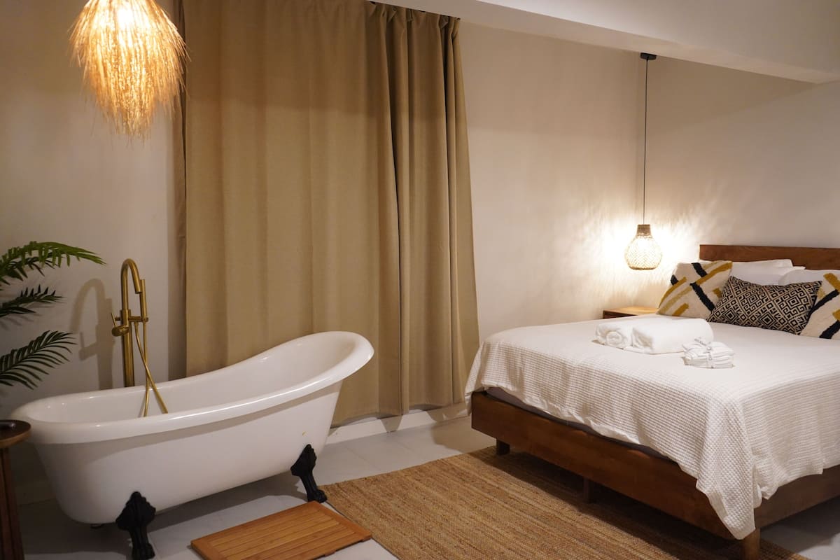 Un dormitorio moderno con una bañera blanca, un cabecero de madera y una mesita de noche con lámpara.