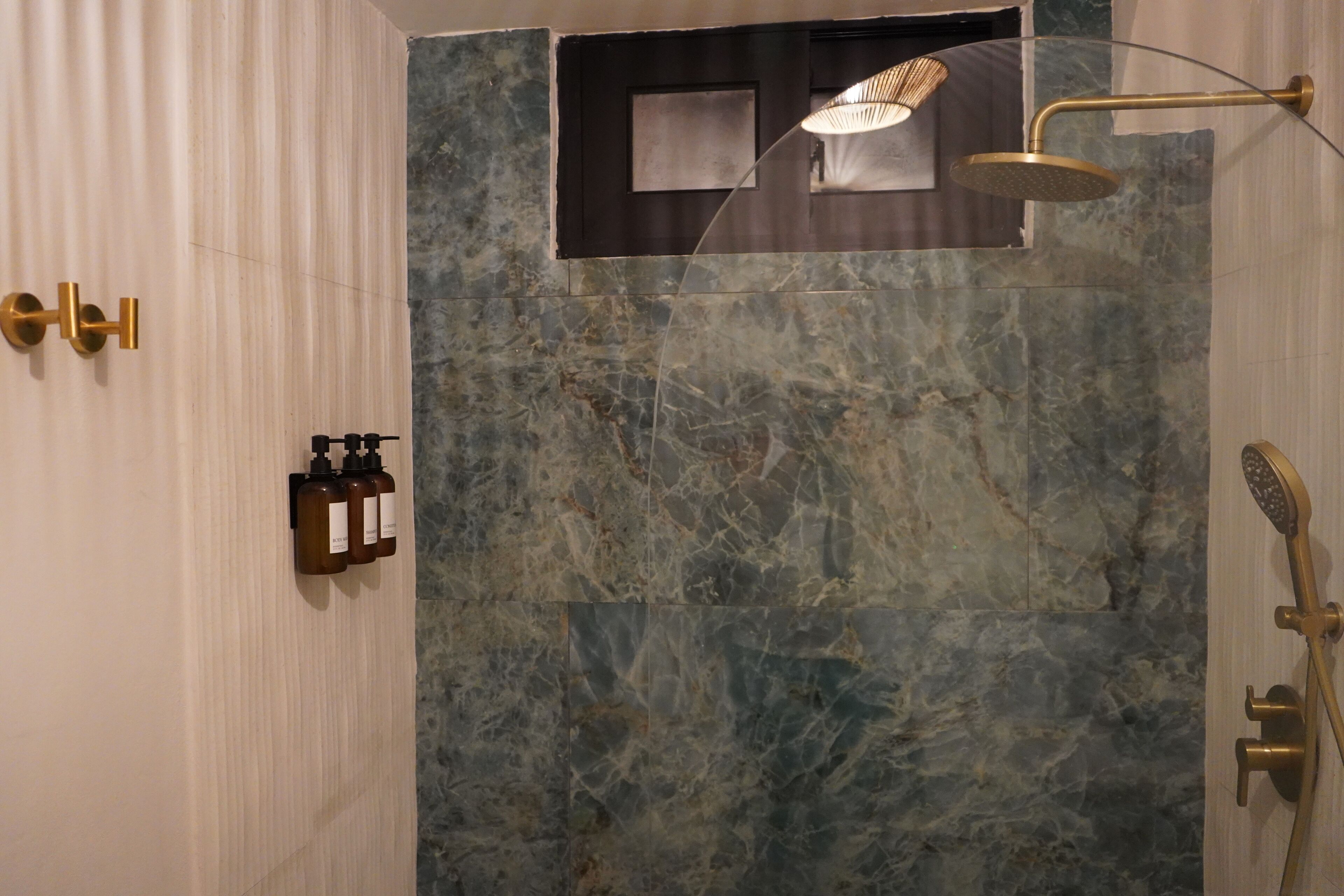 Een moderne badkamer met een marmeren wand, een douche met een gouden kraan en een zeepdispenser op de muur.
