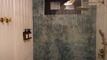 Een moderne badkamer met een marmeren wand, een douche met een gouden kraan en een zeepdispenser op de muur.