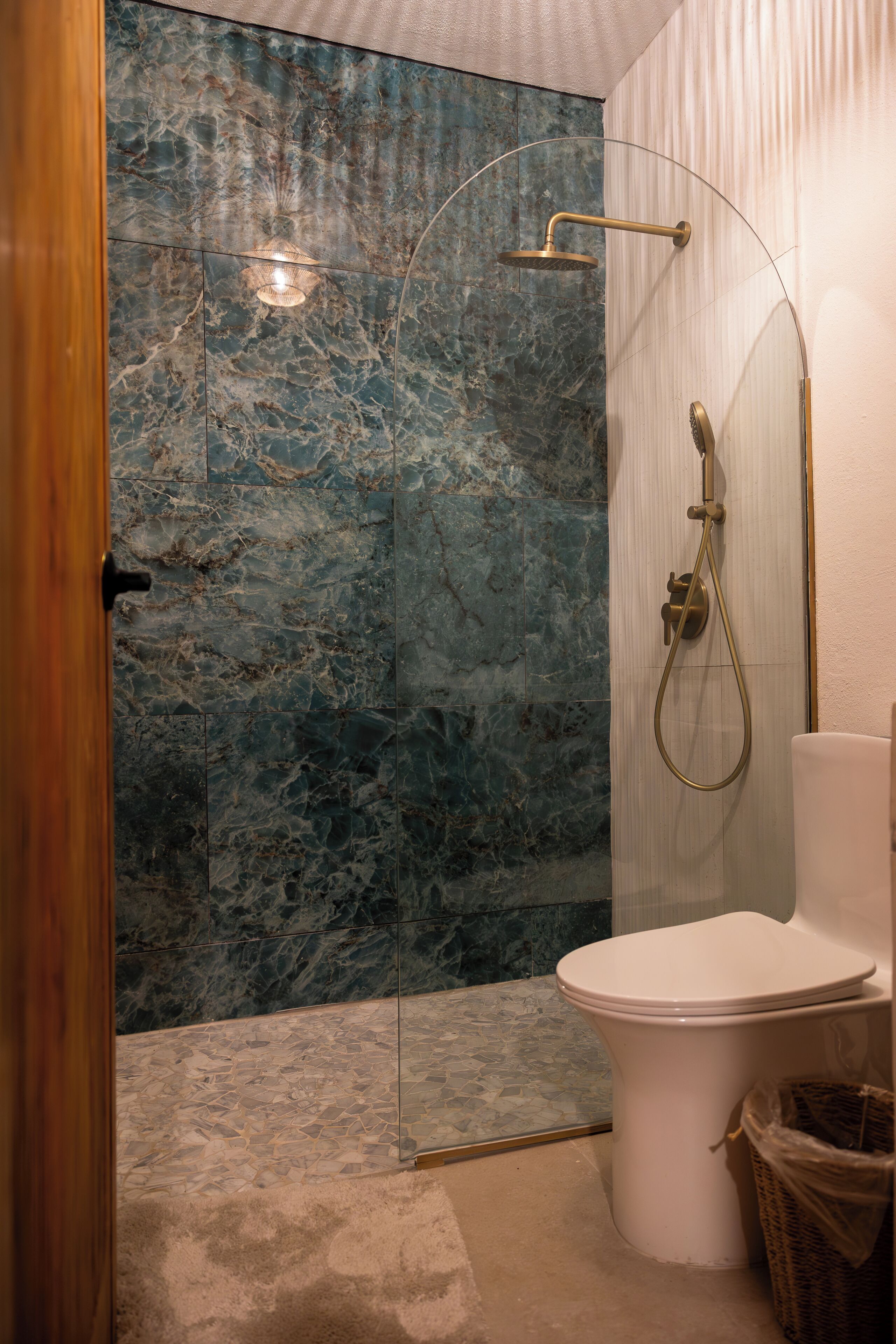 A bathroom with a marble shower wall, a white toilet, and a wicker basket.
