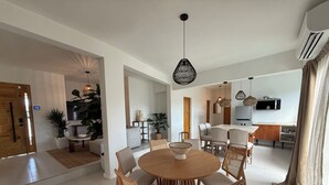 Un comedor moderno con una mesa redonda y sillas, una cocina al fondo y una planta grande en la sala.