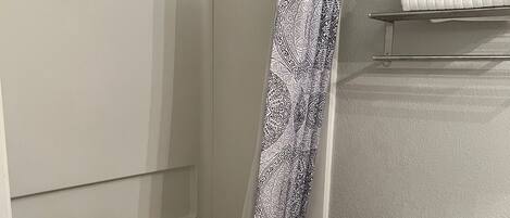 A bathroom with a shower, toilet, and a shelf with towels.