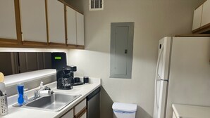 Eine kleine Küche mit Spüle, Kaffeemaschine und Mülleimer.