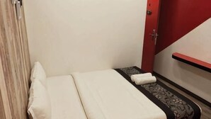 A small, neatly made bed with a white and black bedspread, a red door, and a red wall. - Mango Inn (Semporna)
