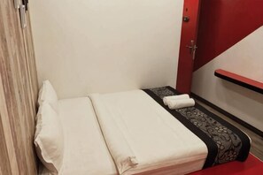 A small, neatly made bed with a white and black bedspread, a red door, and a red wall. - Mango Inn (Semporna)
