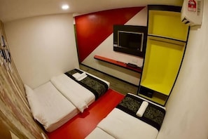 Una habitación pequeña con dos camas, un televisor y un estante amarillo.