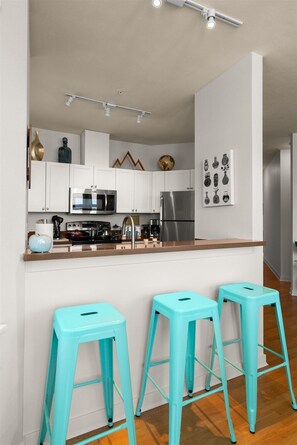 Eine moderne Küche mit weißen Schränken, Edelstahlgeräten und einer Bar mit beigefarbenen Barhocker.