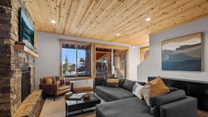 Een moderne woonkamer met een stenen openhaard, houten plafond en grote ramen met uitzicht op het omliggende landschap.