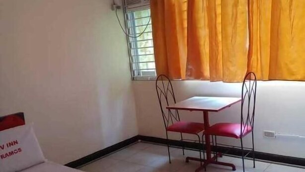 A hotel room with a bed, a small table with two chairs, a window with orange curtains, and an air conditioning unit. - WJV INN RAMOS (Cebu City)