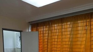 A hotel room with a bed, a bathroom with a toilet, and a window with orange curtains. - WJV INN RAMOS (Cebu City)