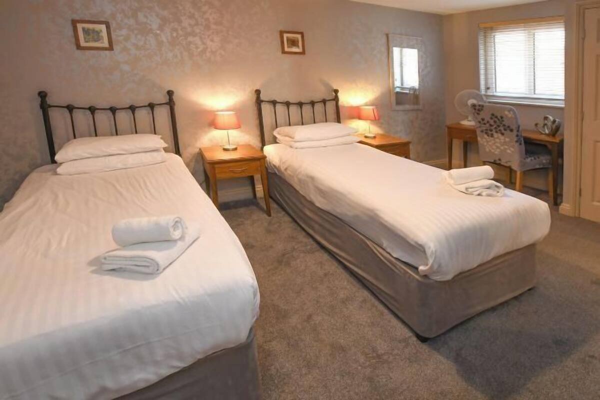 Une chambre avec deux lits simples, des tables de chevet avec des lampes, une chaise et un bureau avec une autre chaise.