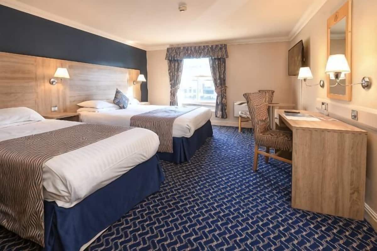 Une chambre d’hôtel avec deux lits, un bureau, une chaise et un grand miroir.