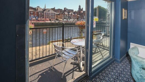 Un balcon avec une table et des chaises, une vue sur une rivière et des bâtiments en arrière-plan.