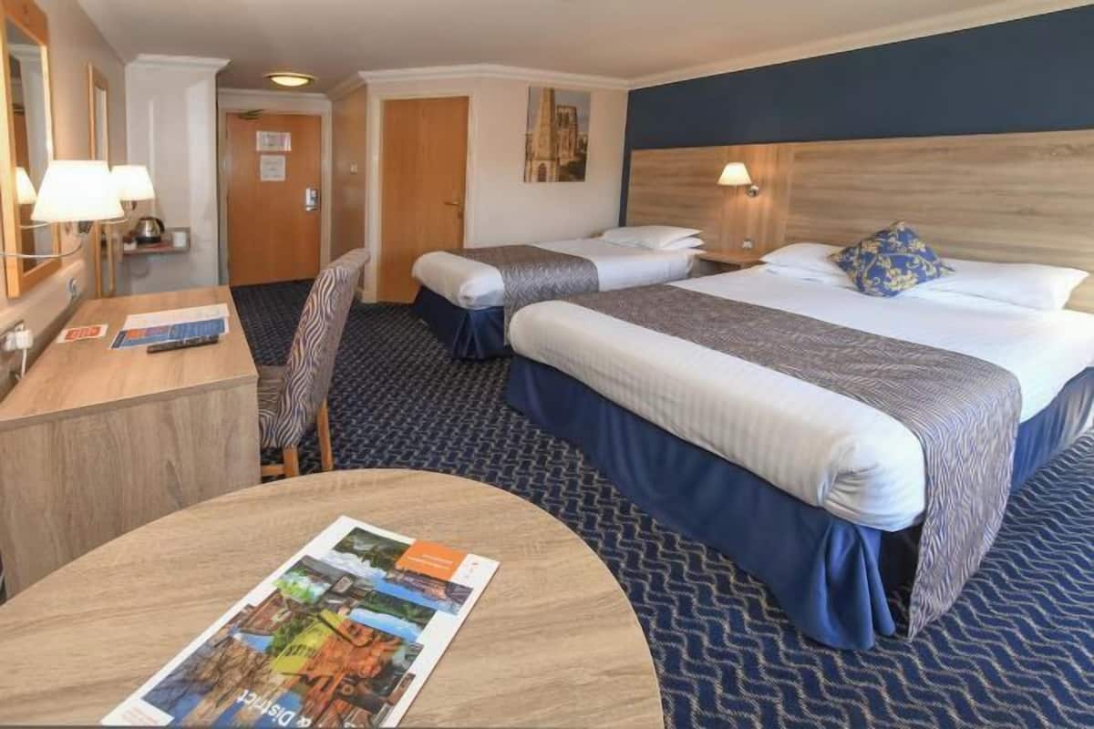 Une chambre d’hôtel avec deux lits, un bureau, une chaise et une table ronde avec un magazine.