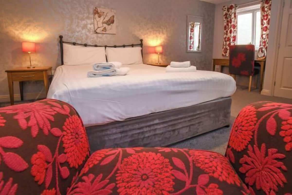 Une chambre avec un grand lit, deux lampes de chevet, une chaise et une fenêtre avec des rideaux.
