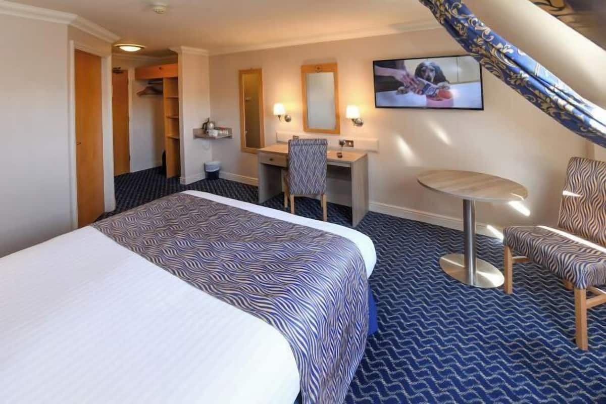 Une chambre d’hôtel avec un grand lit, un bureau avec une chaise, une petite table ronde, un miroir et un téléviseur.