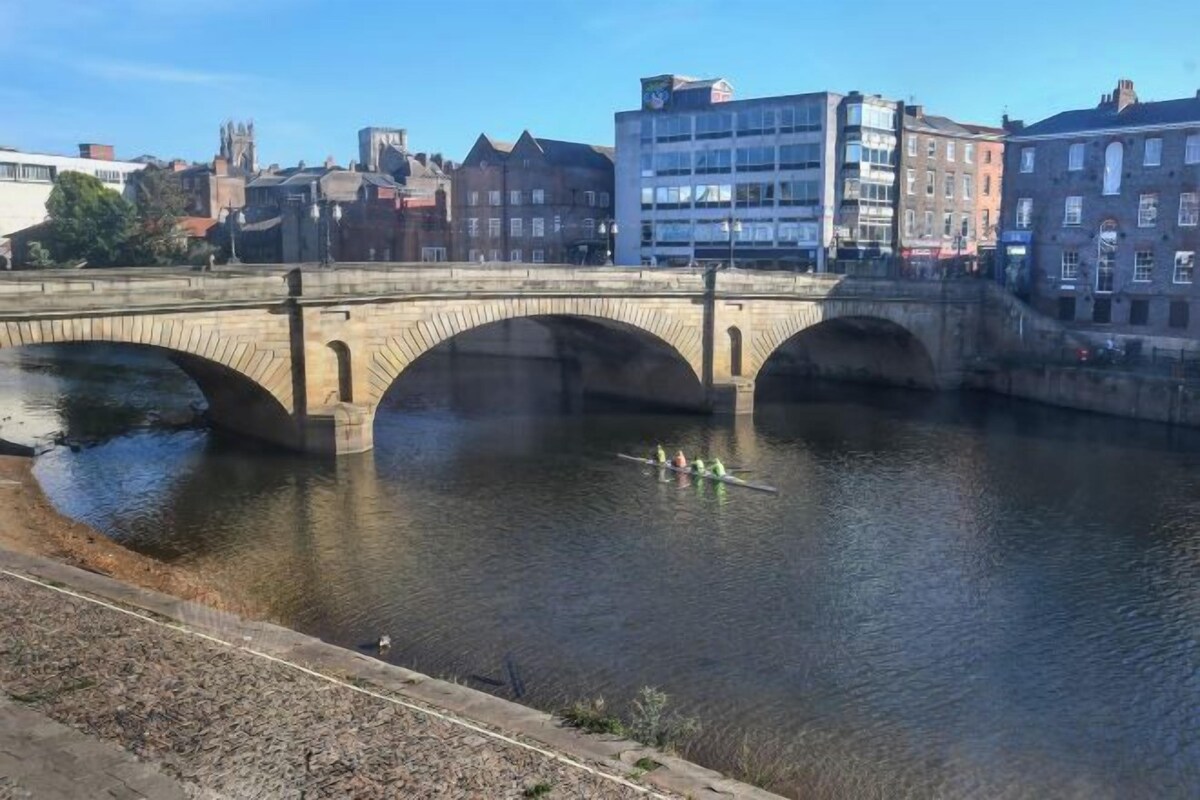 Un pont de pierre enjambe une rivière, avec des bâtiments visibles en arrière-plan.