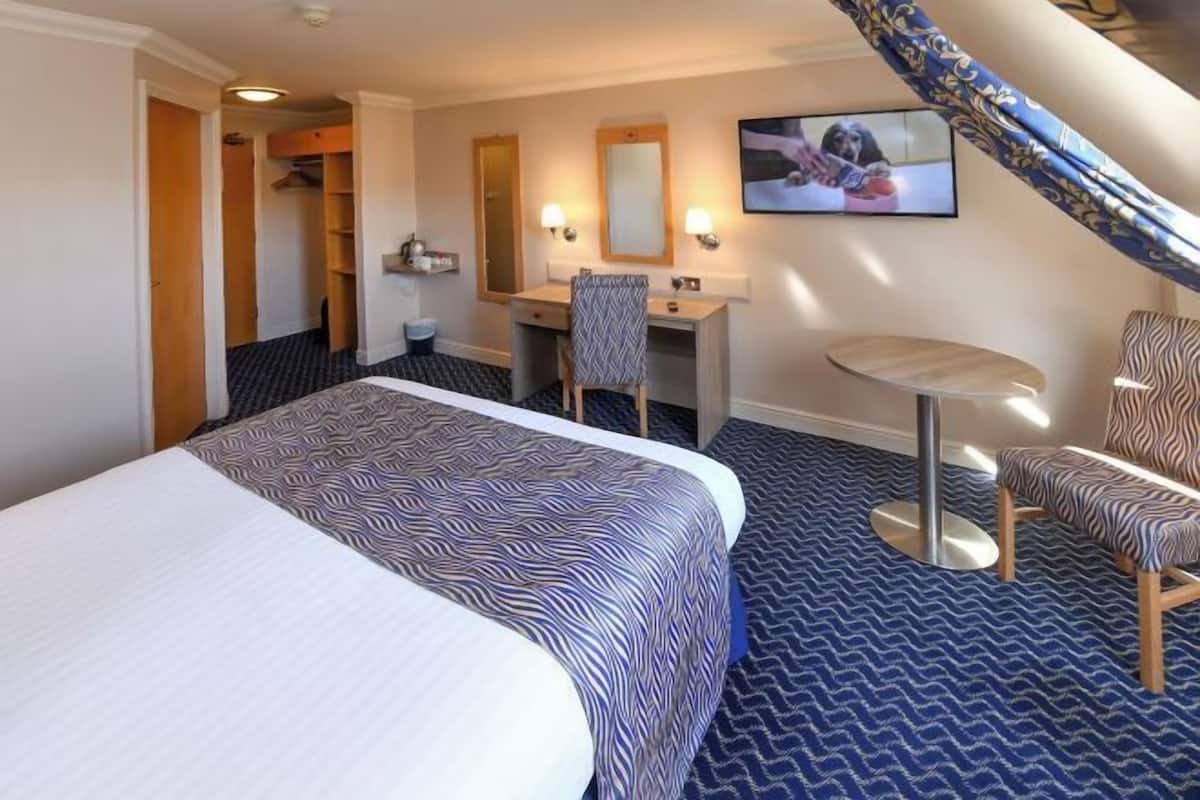 Une chambre d’hôtel avec un lit, un bureau, une chaise et une petite table ronde.