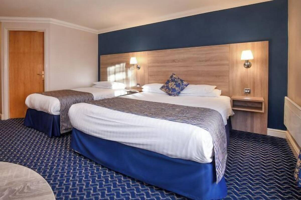 Une chambre d’hôtel avec deux lits, une tête de lit en bois, des lampes de chevet et une moquette à motifs.
