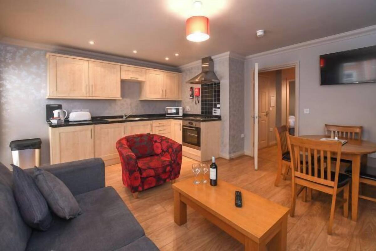 Un espace de vie compact comprenant un coin cuisine, un coin repas et un coin salon avec un canapé et un fauteuil rouge.