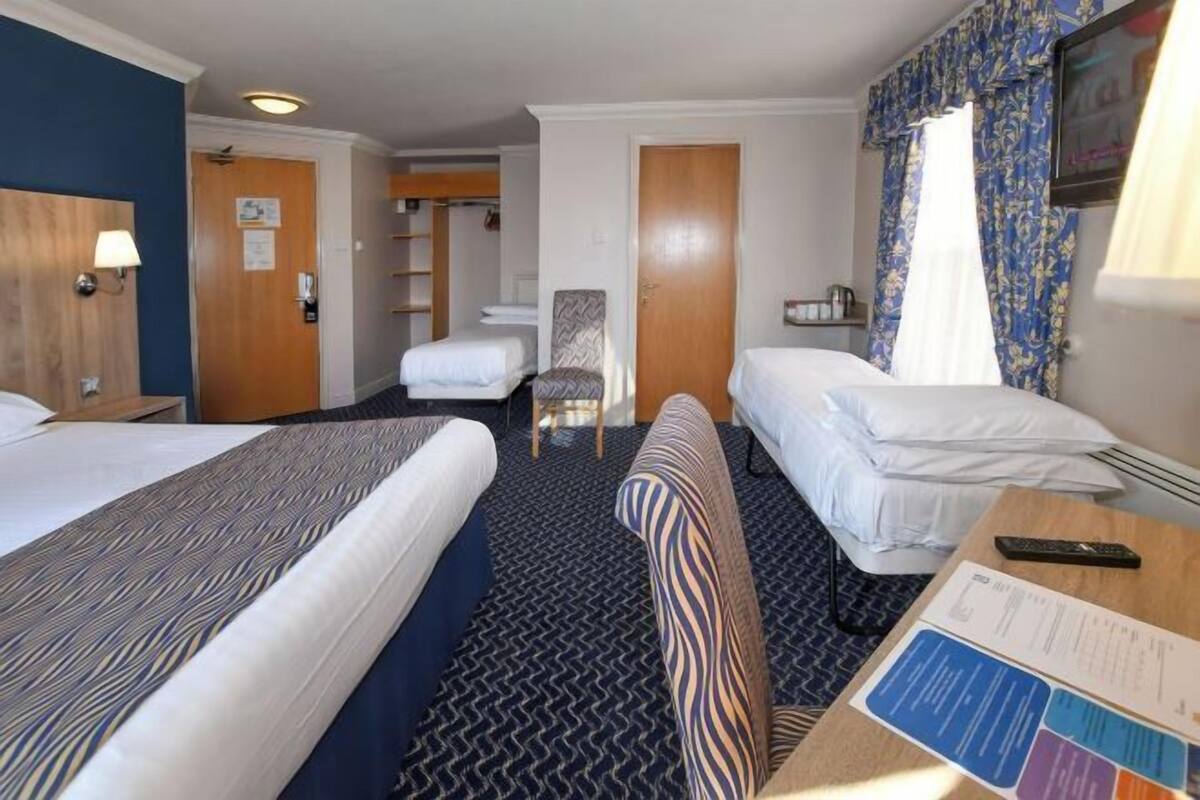 Une chambre d’hôtel avec deux lits, un bureau, une chaise et une petite table avec une télécommande.