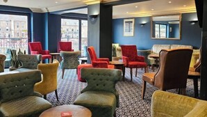 Un hall d’hôtel aménagé avec un mélange de fauteuils et de canapés, un sol à motifs et de grandes fenêtres donnant sur la ville.