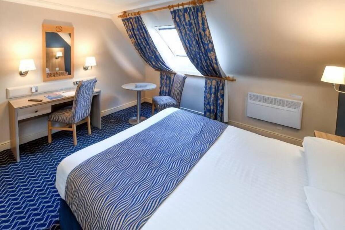 Une chambre d’hôtel avec un lit, un bureau, une chaise et une petite table.