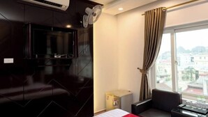 Une chambre d’hôtel avec un lit, un téléviseur fixé au mur, un ventilateur de plafond, une fenêtre avec des rideaux et une vue sur le paysage urbain.