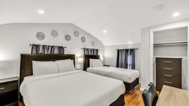 A hotel room with two beds, a wooden floor, a closet, and a dining table. - 3 Bed 1 Bath (Cambridge)