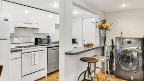 A modern kitchen with white cabinets, a stove, microwave, and a washing machine. - 3 Bed 1 Bath (Cambridge)