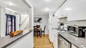 A modern kitchen with white cabinets, a microwave, and a dishwasher. - 3 Bed 1 Bath (Cambridge)