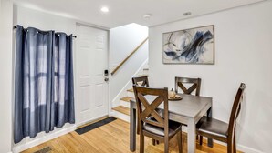 A dining area with a wooden table and chairs, a blue curtain, a white door, and a staircase. - 3 Bed 1 Bath (Cambridge)