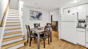 A modern kitchen with white cabinets, a white refrigerator, and a dining area with a wooden table and chairs. - 3 Bed 1 Bath (Cambridge)