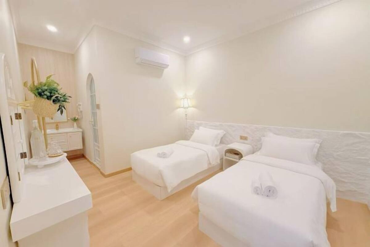 A hotel room with two beds, a bedside table, a small nightstand, a mirror, a wall-mounted air conditioner, and a wall-mounted lamp.