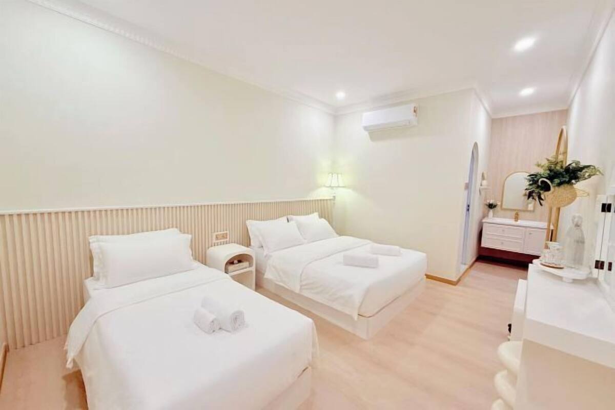 A hotel room with two beds, a bedside table, a mirror, a dresser, and a plant.
