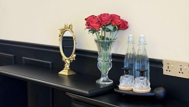 A black countertop with a gold-framed mirror, a clear vase with red roses, and two clear glass bottles with black bases. - The Cozy Cottage Semporna (Semporna)