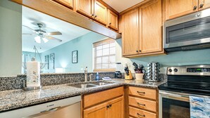 A kitchen with wooden cabinets, a granite countertop, a Bosch dishwasher, a stove, and a microwave. - Steps to Sand: Condo w/ Pool Access in Cocoa Beach (Cocoa Beach)