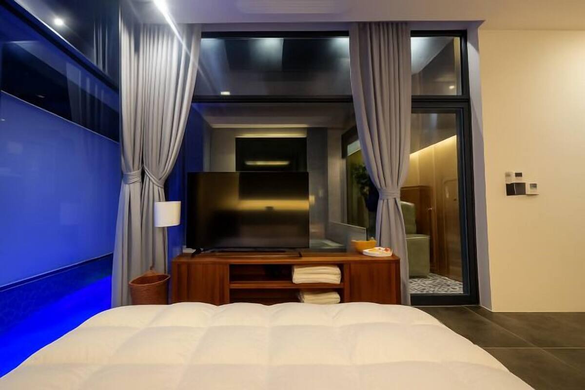 Ein modernes Hotelzimmer mit Bett, Fernseher, kleinem Tisch und einer Schiebetür zum Badezimmer.
