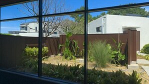 A modern building with large windows, a fenced garden, and a clear blue sky. - Dodu trophycal Pool Villa near by Airport (Jeju)