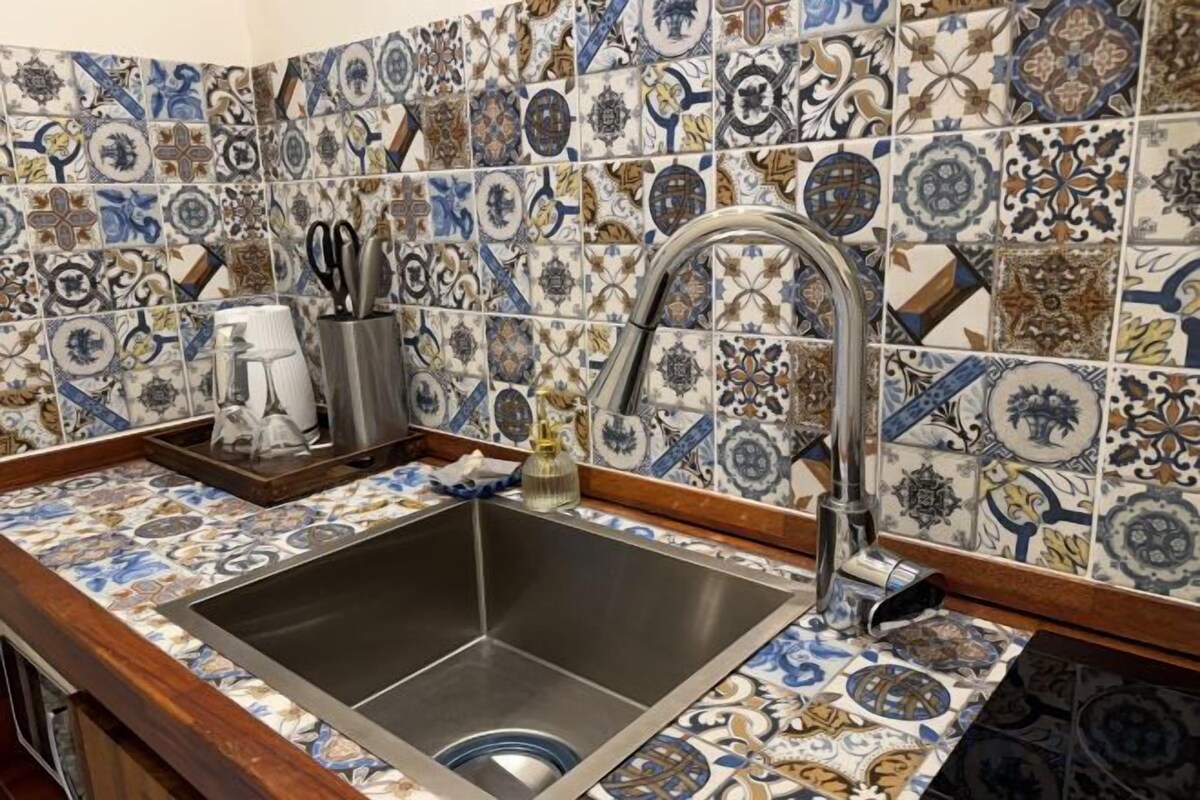 A kitchen with a tiled backsplash, a stainless steel sink, and a wooden countertop.