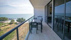 Un balcon avec une table et des chaises, donnant sur une étendue d’eau et sur de la verdure.